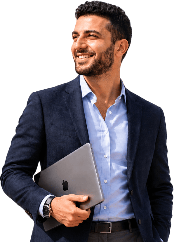 A smiling man with short dark hair and a beard holds a closed laptop under his arm. He is wearing a dark blazer, light blue dress shirt, and a smartwatch, standing against a plain white background.